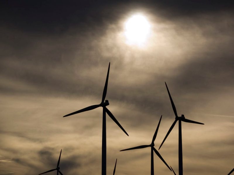 wind turbine blades are silhouetted against a cloudy sky