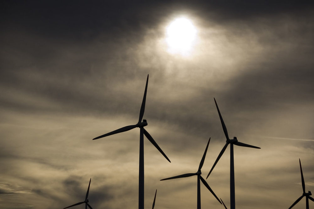 wind turbine blades are silhouetted against a cloudy sky