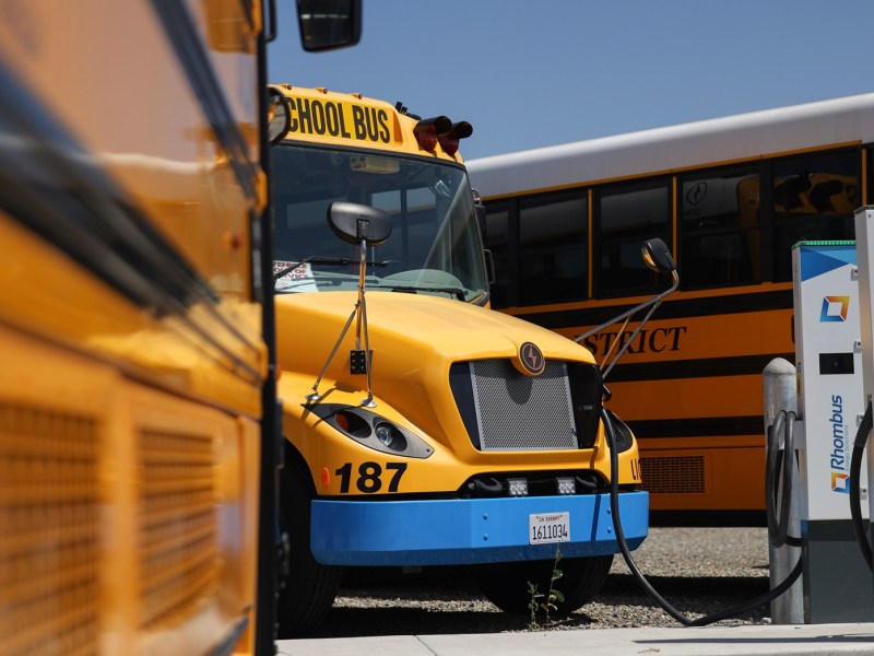 A yellow electric school bus is plugged into a charging station.