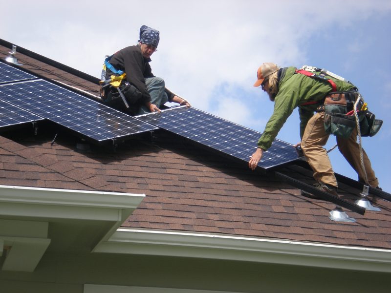 Workers install solar panels on a roof.