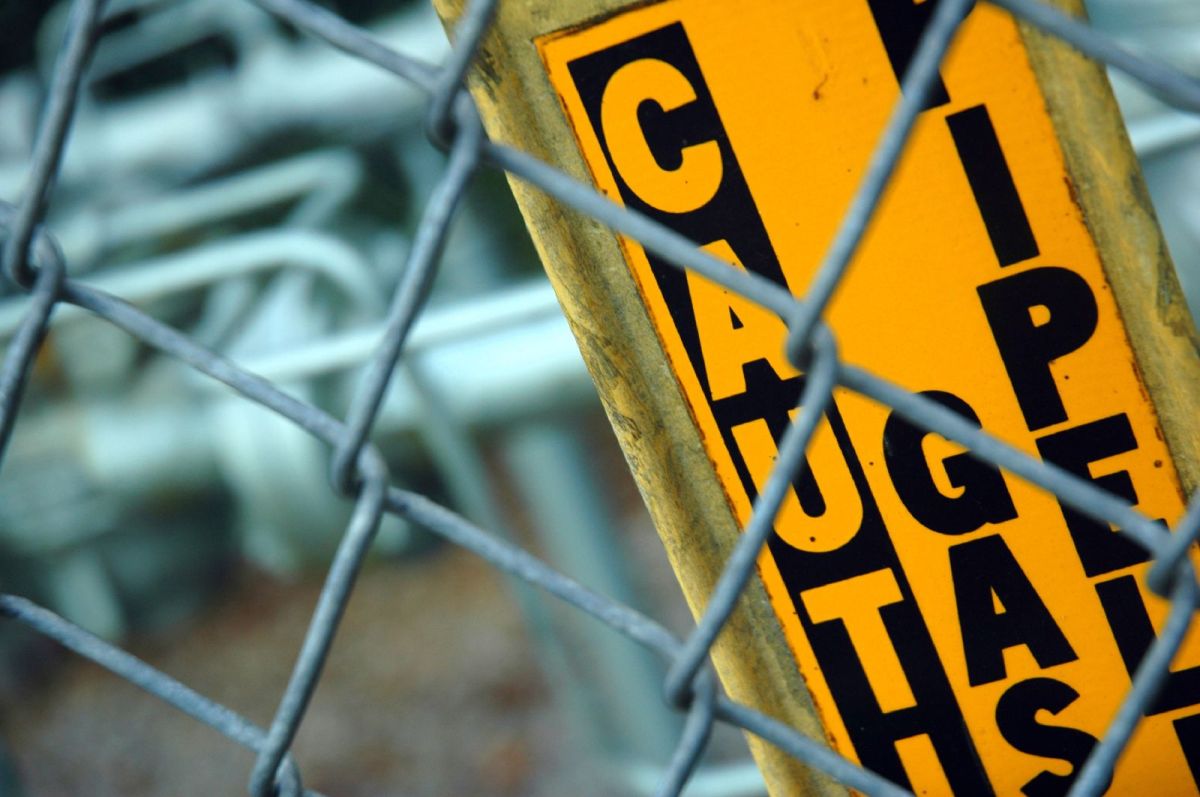 A caution gas pipeline sign behind a chain link fence.