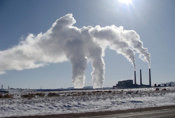 Smokestacks in the distance against a grey-blue sky billow white smoke.