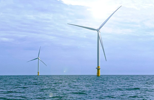 One wind turbine stands in ocean against a cloudy sky in the foreground, and another stands in the back.