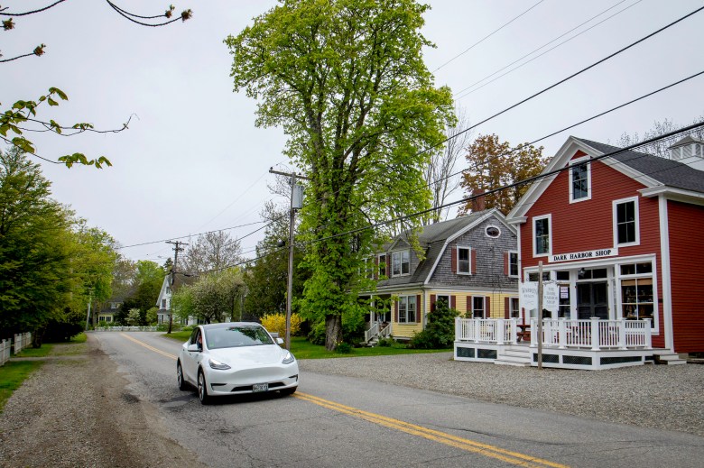 A Tesla drives on a road through a small town in Maine.