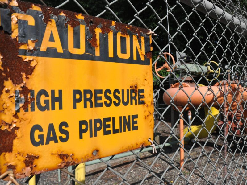 A rusted sign on a chain link fence reads "caution, high press gas pipeline"