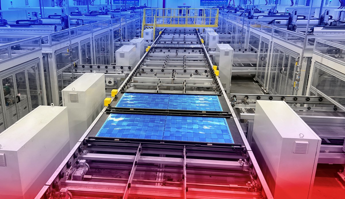 A factory filled with clean white structures produces solar panels, visible in blue at the front of the picture.