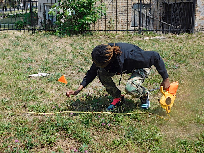 A person holding a measuring tape plants an orange marker flag in a vacant lot in Chicago.