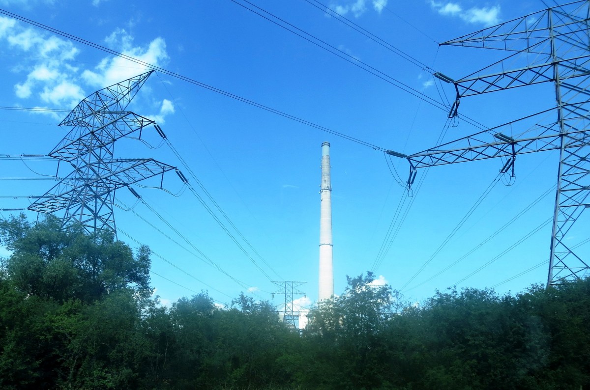 A smokestack against a blue sky with electrical transmission towers in the foreground.