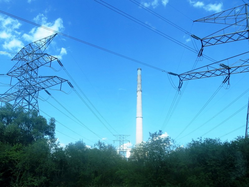 A smokestack against a blue sky with electrical transmission towers in the foreground.