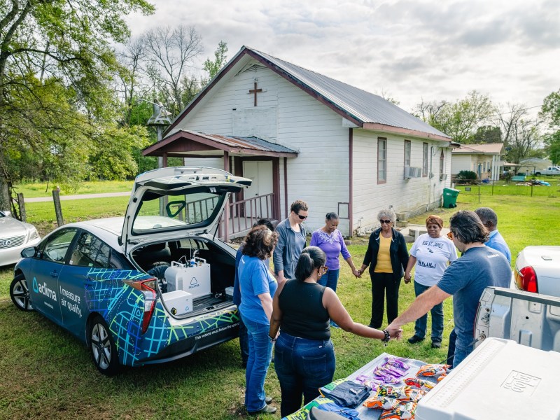 Pastor Harry Joseph leads community members, members of the Louisiana Environmental Action Network and Aclima scientist Aja Ellis in prayer on March 16, 2024 beside the Aclima air-monitoring car in front of the Mount Triumph Baptist Church in St. James Parish, La.