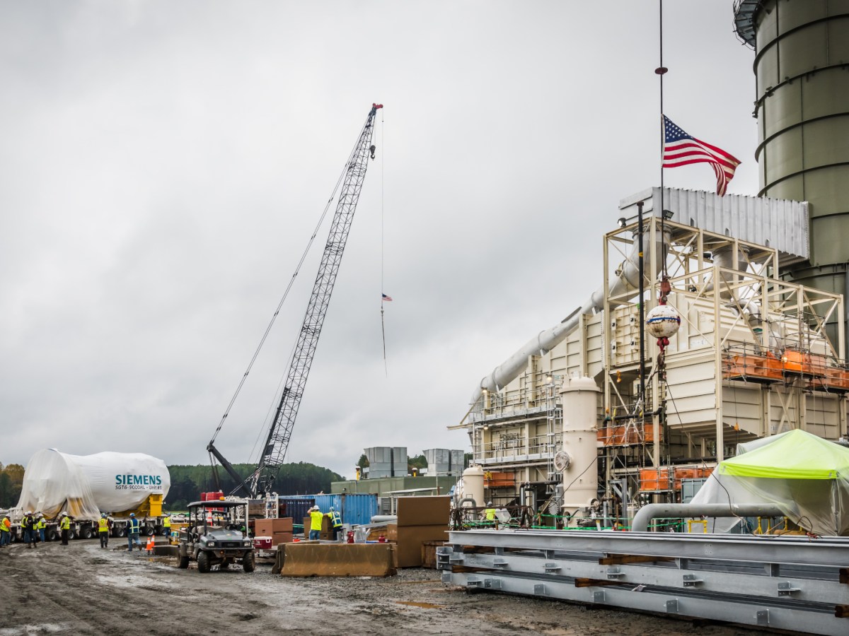 A crane and workers at a natural gas power plant as a new gas turbine is delivered.