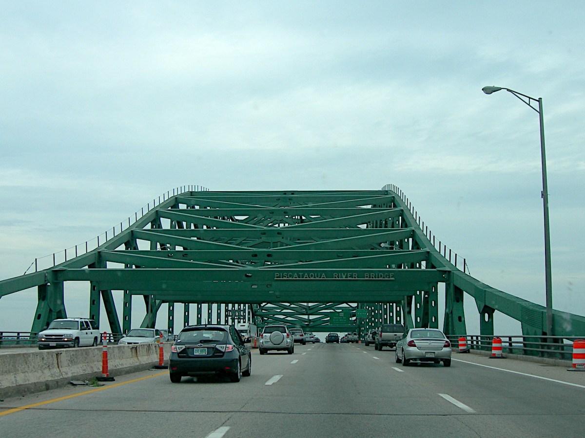 Cars travel across a highway bridge topped with a green girder structure