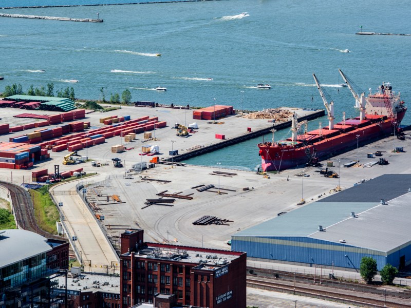 Overhead view of the Port of Cleveland, showing a docked ship and shipping containers and other materials on the dock.