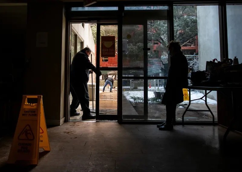 Two people wait inside a dark building in Texas. Snow is visible outside.