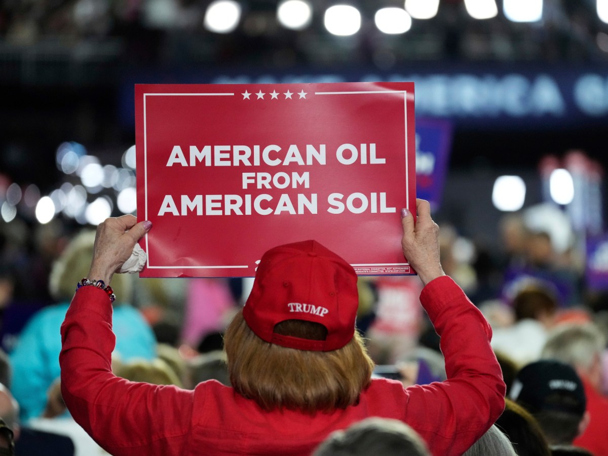 A person wearing a red Trump hat holds a sign reading "American oil from American soil" at the Republican National Convention.