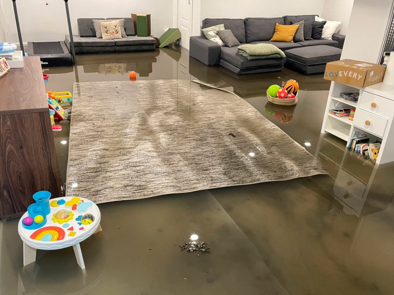 A basement apartment is flooded in several inches of dirty water, ruining a couch, dresser, rug and other furniture.