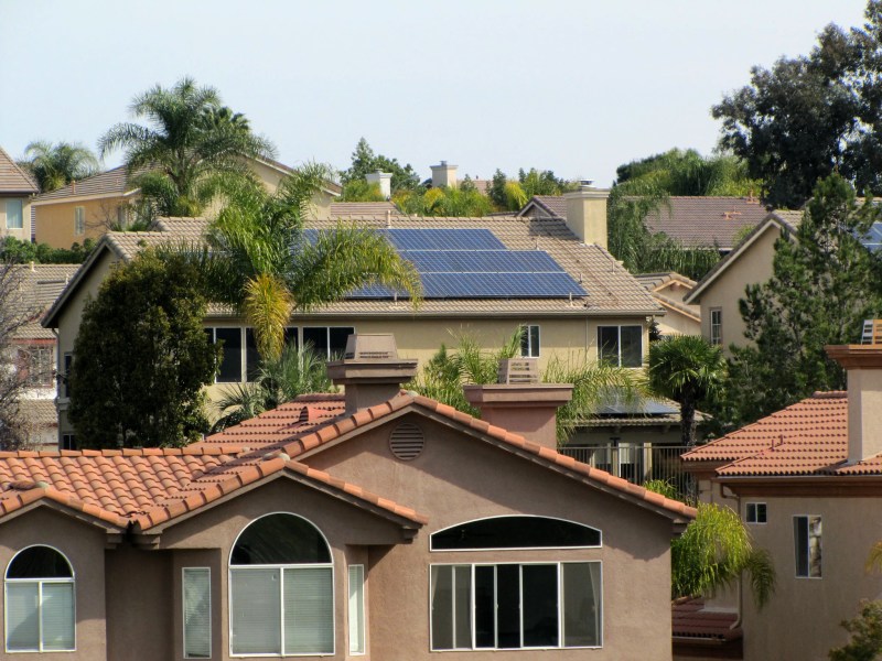 Houses in California with Spanish tiles and palm trees, with solar panels on one house.