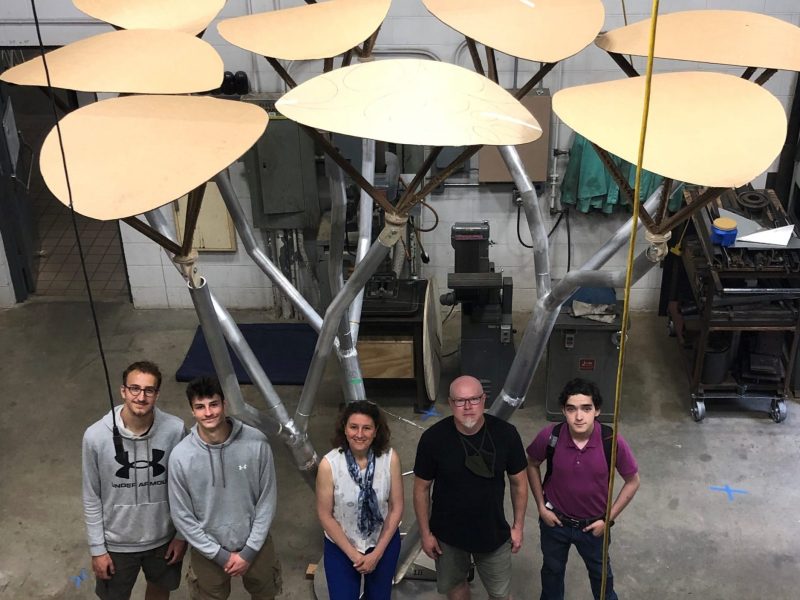 Five people stand under nine aluminum leaves that will soon be outfitted with solar panels.